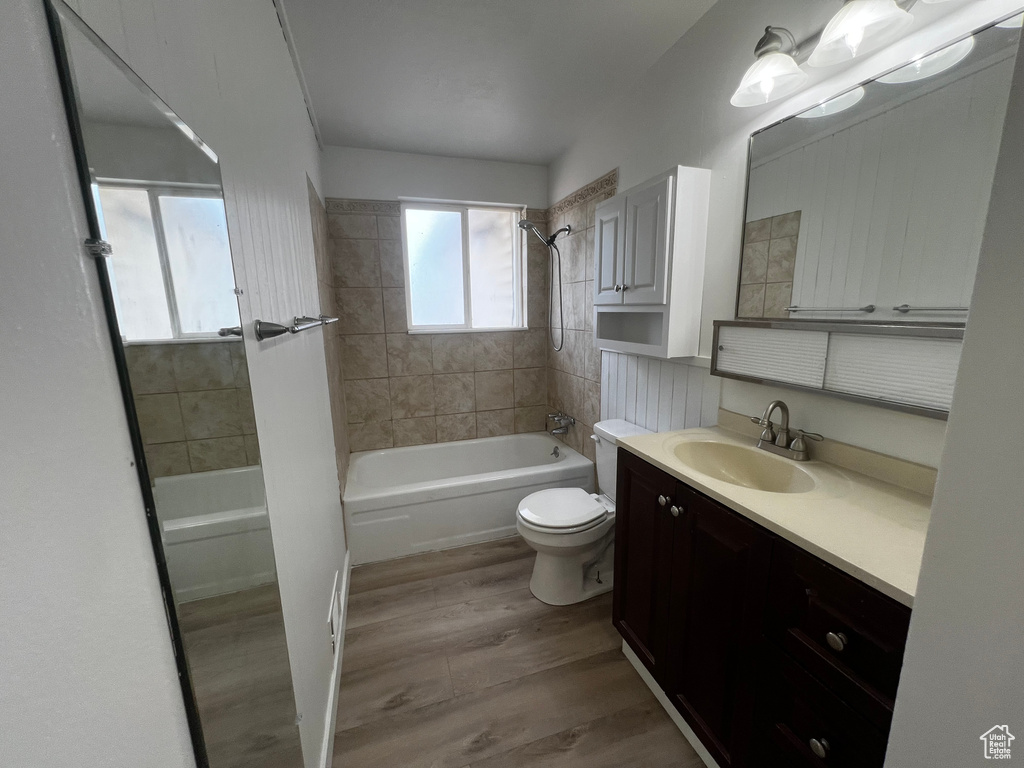 Full bathroom with hardwood / wood-style floors, vanity, tiled shower / bath combo, and toilet