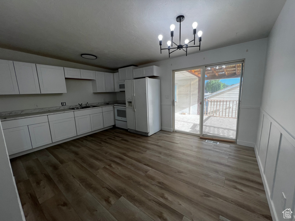 Kitchen with white cabinetry, hardwood / wood-style flooring, a chandelier, white appliances, and sink