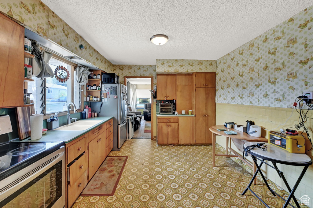 Kitchen featuring light tile patterned flooring, stainless steel appliances, sink, and a textured ceiling