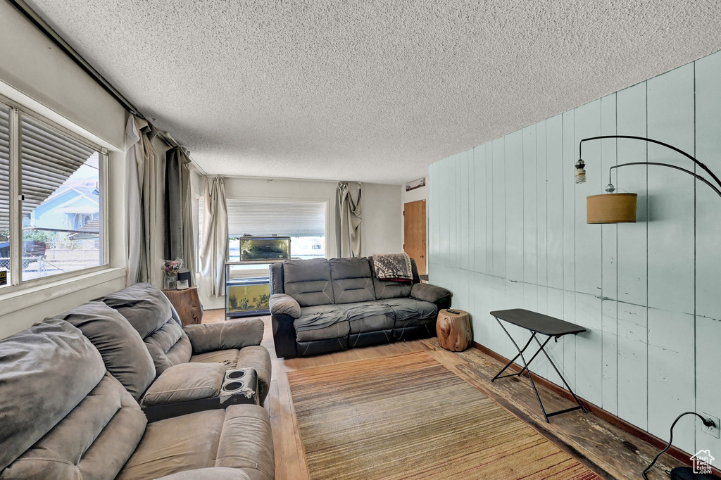 Living room featuring a textured ceiling, wooden walls, and light hardwood / wood-style floors