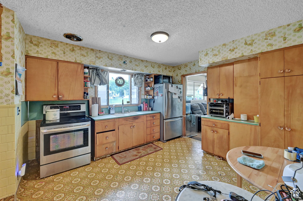 Kitchen with light tile patterned flooring, stainless steel appliances, sink, and a textured ceiling