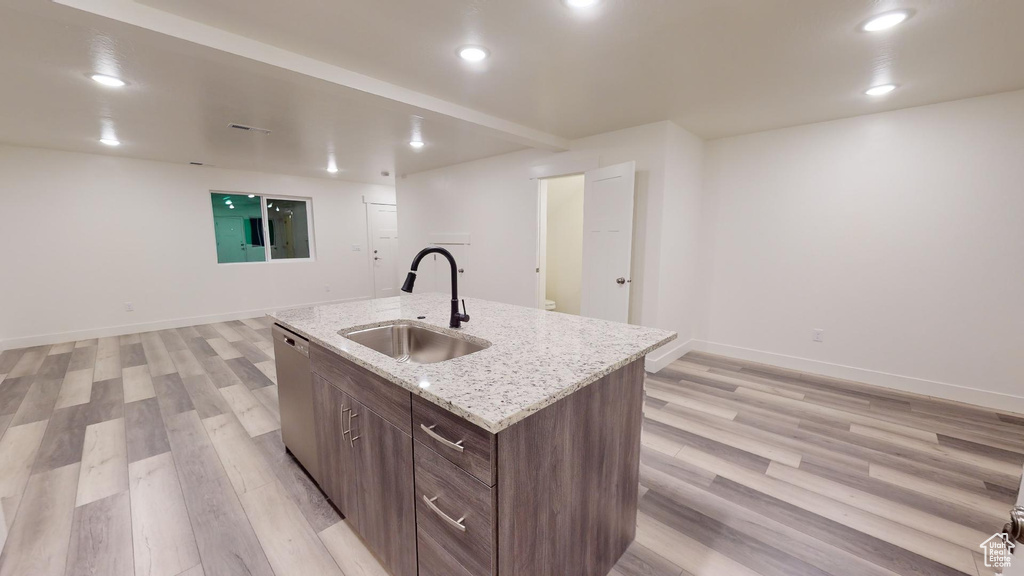 Kitchen with light hardwood / wood-style flooring, light stone counters, a kitchen island with sink, stainless steel dishwasher, and sink