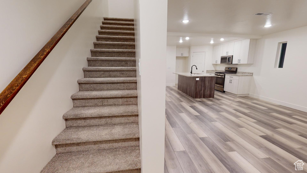 Stairway with light hardwood / wood-style floors and sink