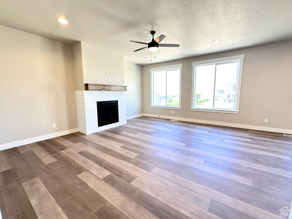 Unfurnished living room with a textured ceiling, ceiling fan, hardwood / wood-style flooring, and a fireplace