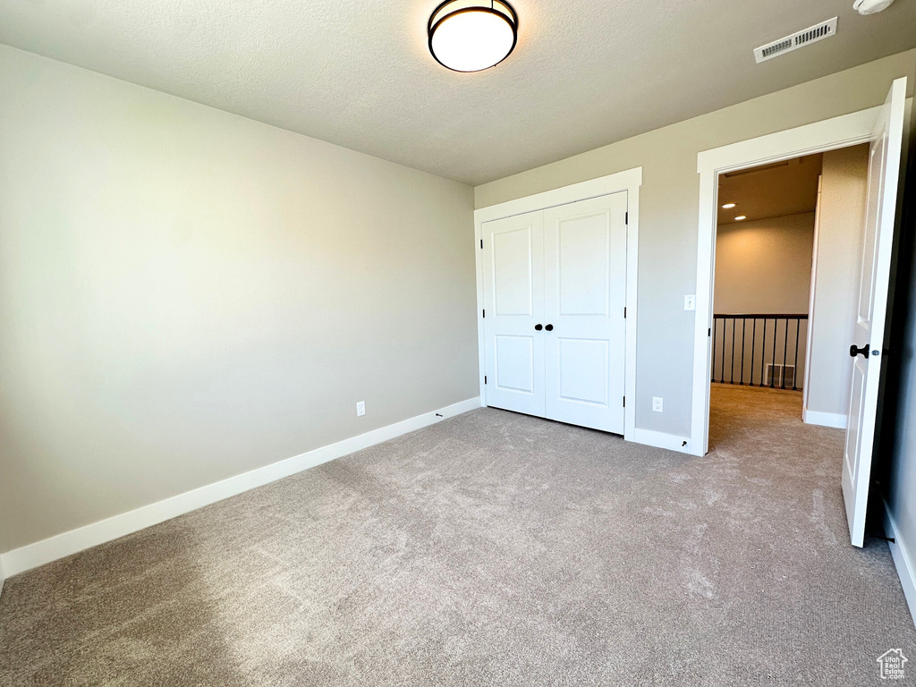 Unfurnished bedroom with a textured ceiling, light colored carpet, and a closet