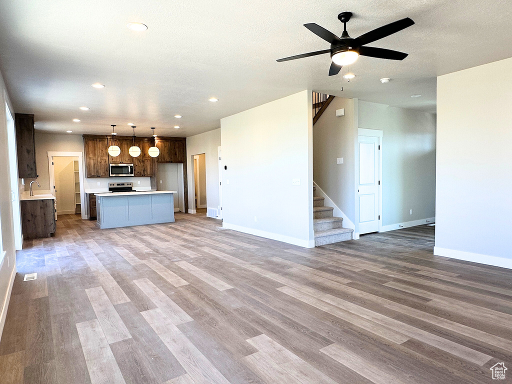 Unfurnished living room with a textured ceiling, ceiling fan, sink, and light hardwood / wood-style floors