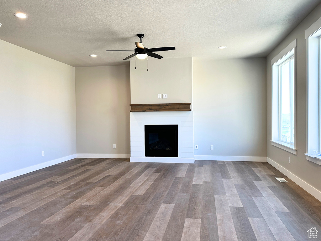 Unfurnished living room featuring a fireplace, a textured ceiling, hardwood / wood-style floors, and ceiling fan