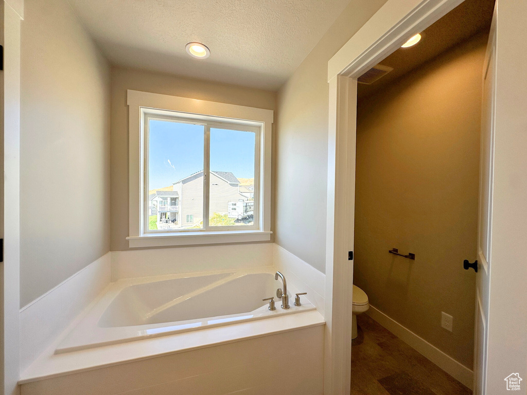 Bathroom featuring toilet, hardwood / wood-style floors, a bath, and a textured ceiling