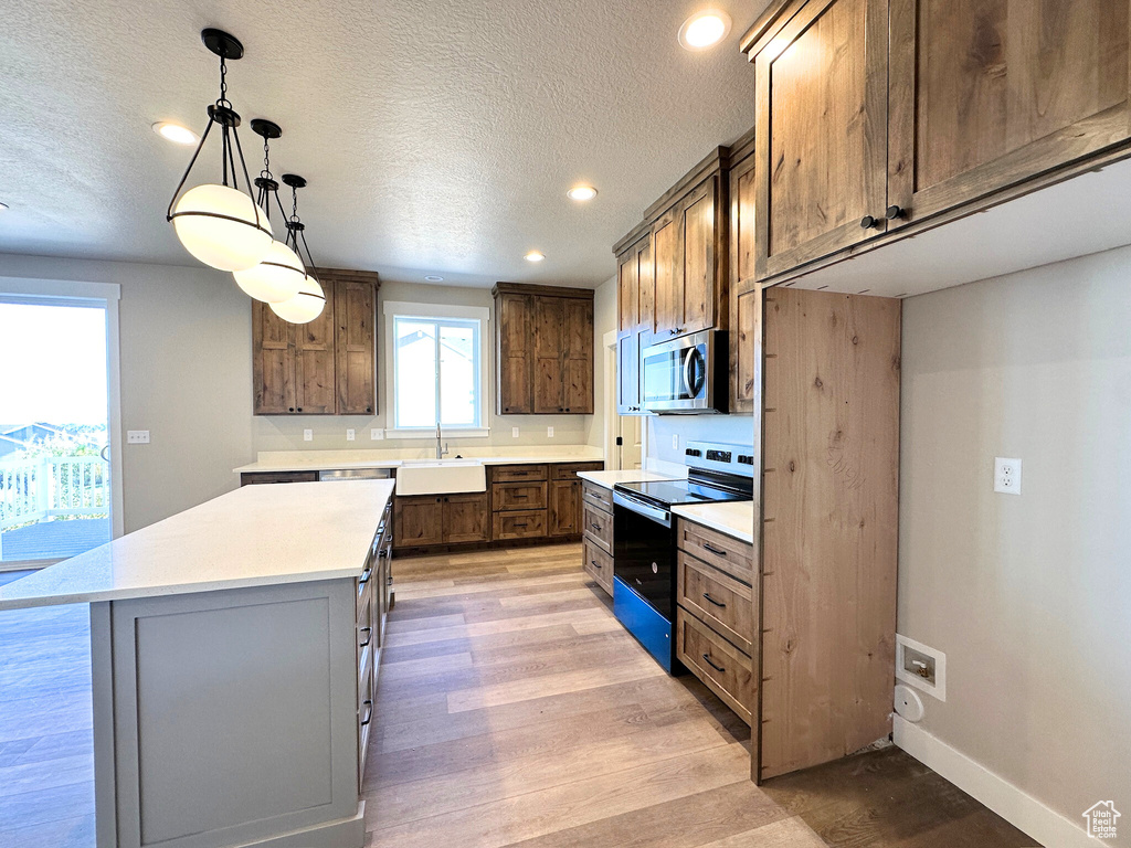 Kitchen with black range with electric stovetop, a kitchen island, light hardwood / wood-style flooring, hanging light fixtures, and sink