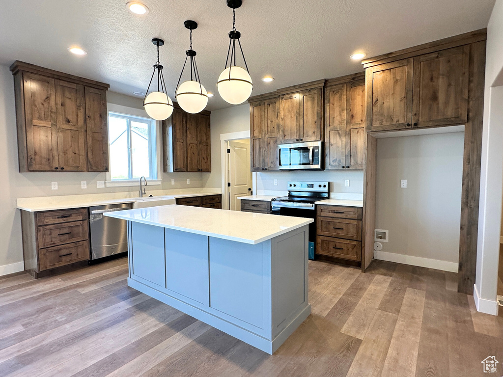 Kitchen with appliances with stainless steel finishes, a kitchen island, pendant lighting, and a textured ceiling