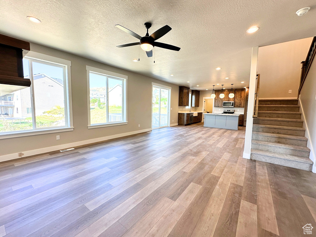 Unfurnished living room with a textured ceiling, plenty of natural light, ceiling fan, and hardwood / wood-style floors