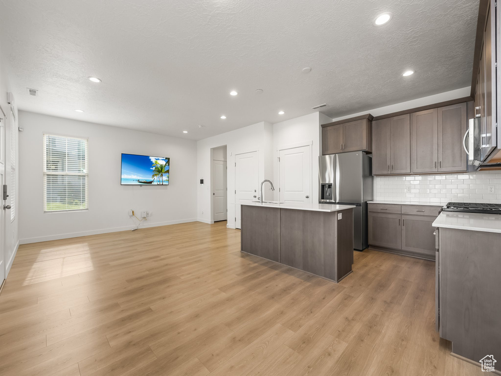 Kitchen featuring light wood-type flooring, a kitchen island with sink, decorative backsplash, stainless steel fridge, and sink