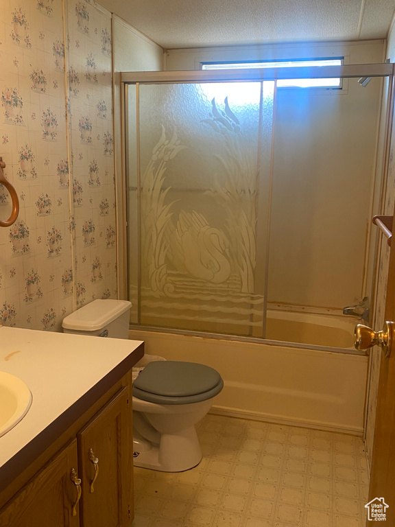 Full bathroom with a textured ceiling, combined bath / shower with glass door, toilet, vanity, and tile patterned flooring