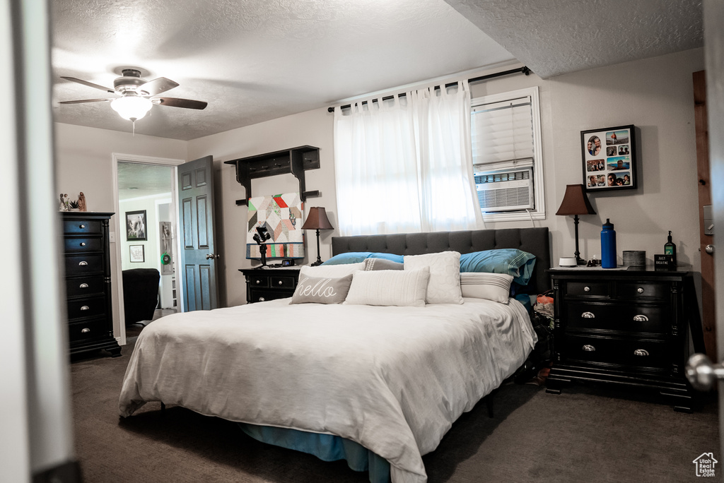 Carpeted bedroom with a textured ceiling, ceiling fan, and cooling unit