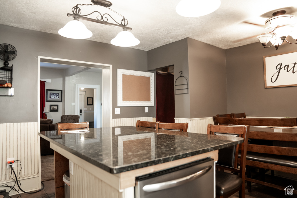 Kitchen featuring pendant lighting, dark stone countertops, a center island, and dishwasher