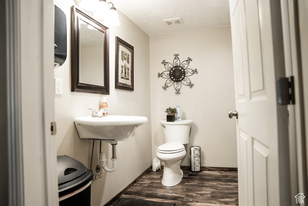 Bathroom featuring wood-type flooring, toilet, sink, and a textured ceiling