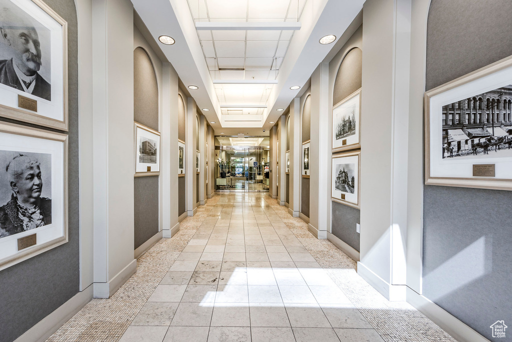 Hallway with light tile patterned flooring and a tray ceiling