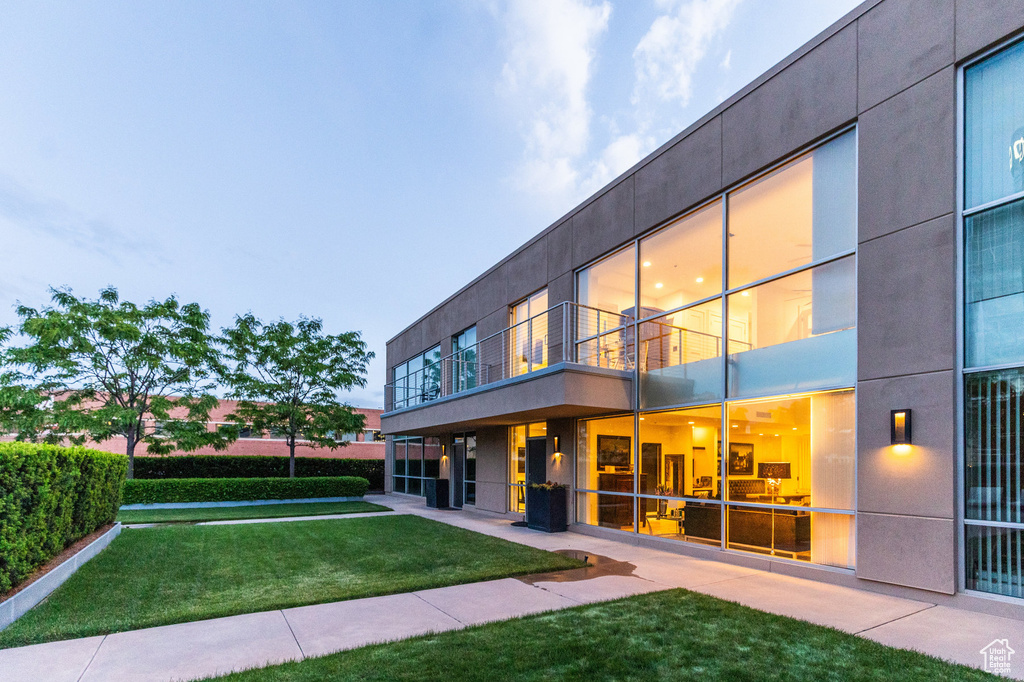 Back house at dusk featuring a lawn and a balcony