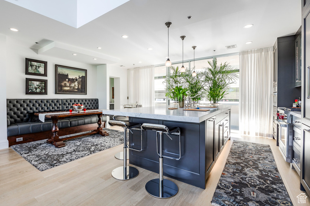 Kitchen with a kitchen island, hanging light fixtures, a kitchen bar, light stone counters, and light hardwood / wood-style floors