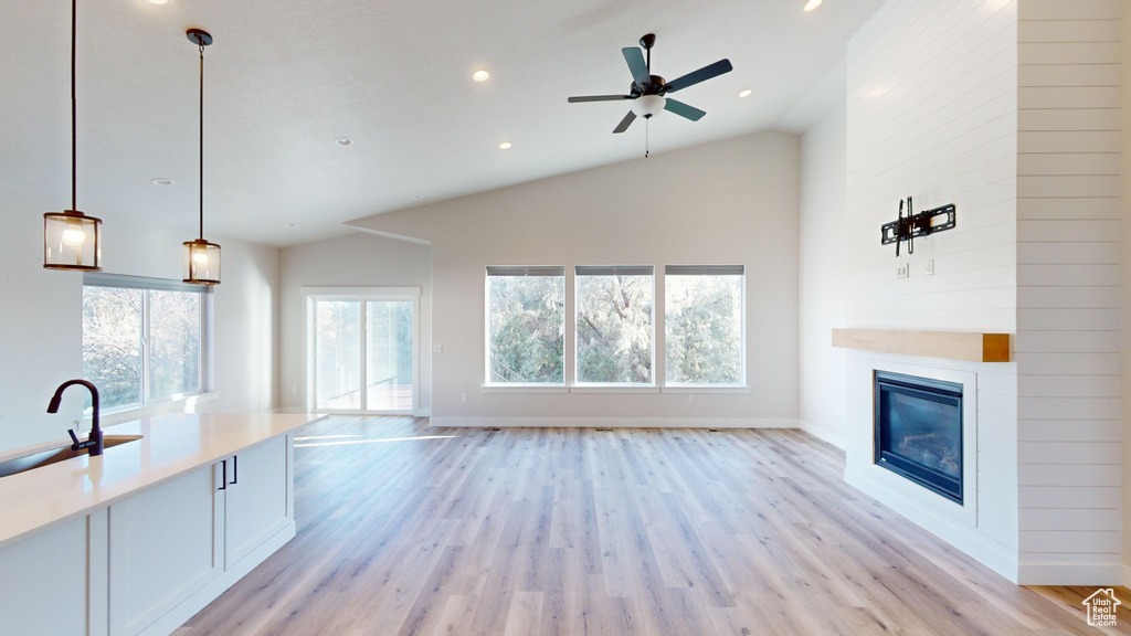 Unfurnished living room with a large fireplace, sink, ceiling fan, and light wood-type flooring