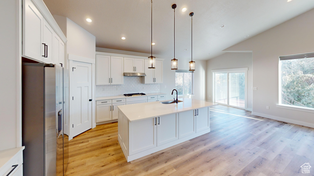 Kitchen featuring lofted ceiling, an island with sink, stainless steel fridge, light wood-type flooring, and pendant lighting