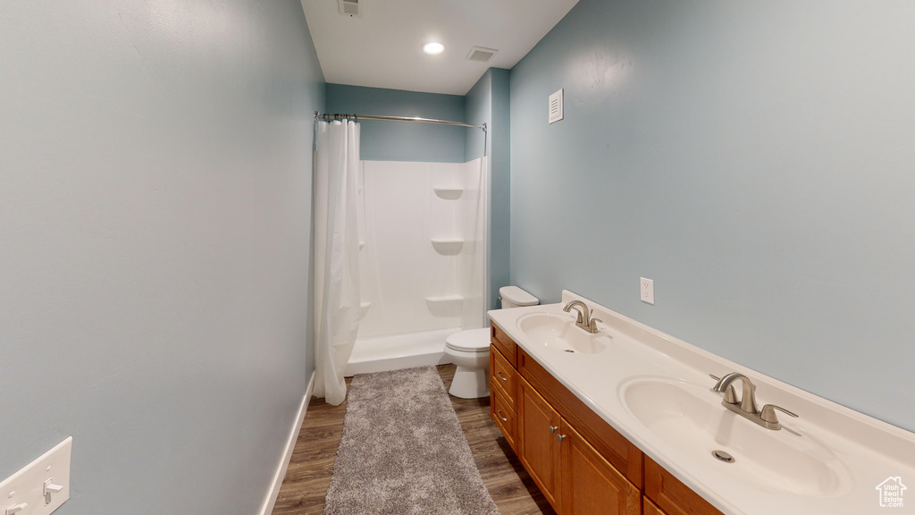 Bathroom featuring dual vanity, a shower with shower curtain, hardwood / wood-style floors, and toilet