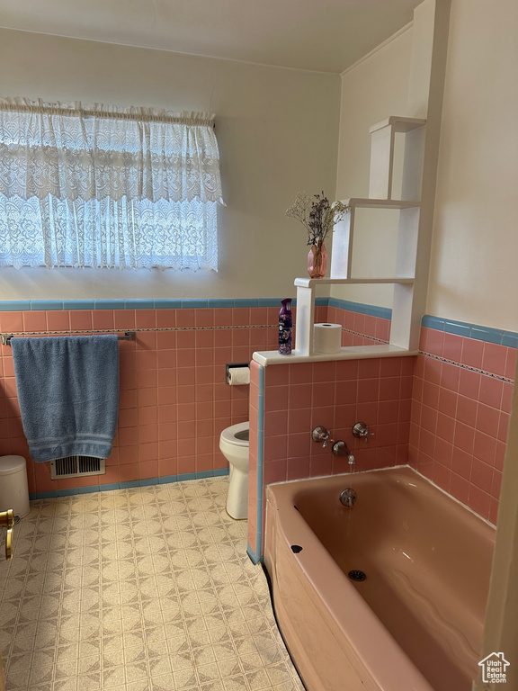 Bathroom with toilet, tile patterned floors, tile walls, and a bathtub