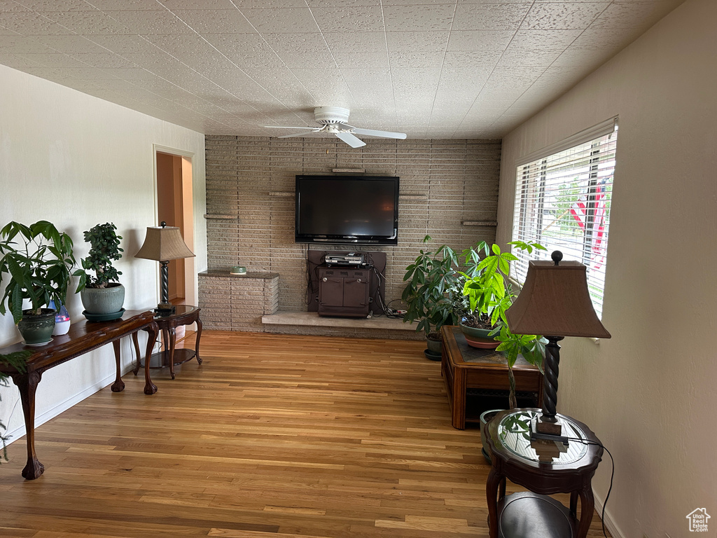 Living room with hardwood / wood-style flooring, brick wall, and ceiling fan