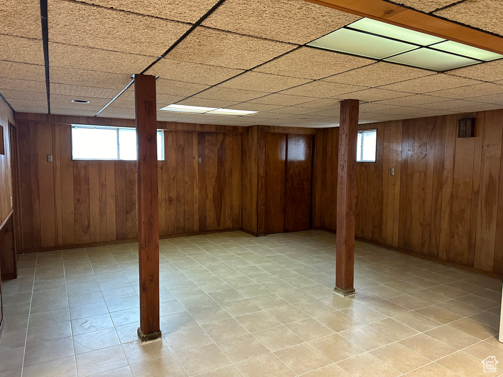 Basement featuring wood walls, a drop ceiling, and plenty of natural light