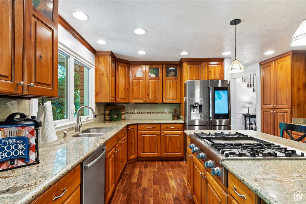 Kitchen featuring dark hardwood / wood-style flooring, light stone countertops, hanging light fixtures, appliances with stainless steel finishes, and sink