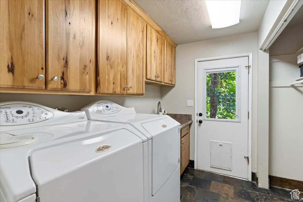 Laundry area with cabinets, washing machine and clothes dryer, dark tile patterned flooring, and a textured ceiling