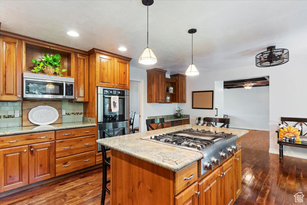 Kitchen featuring ceiling fan, dark hardwood / wood-style floors, a kitchen island, appliances with stainless steel finishes, and backsplash