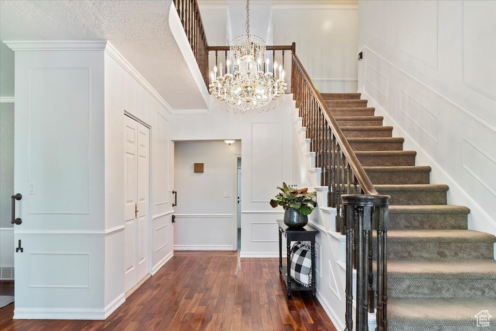 Foyer with an inviting chandelier, a textured ceiling, crown molding, and dark wood-type flooring