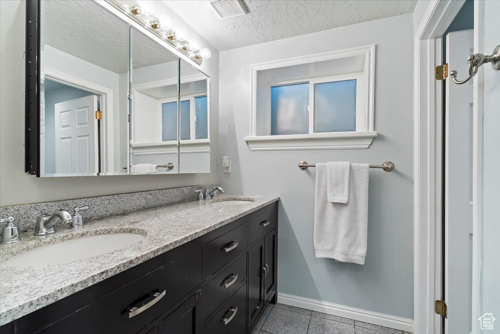 Bathroom with tile patterned flooring, double sink vanity, and a textured ceiling