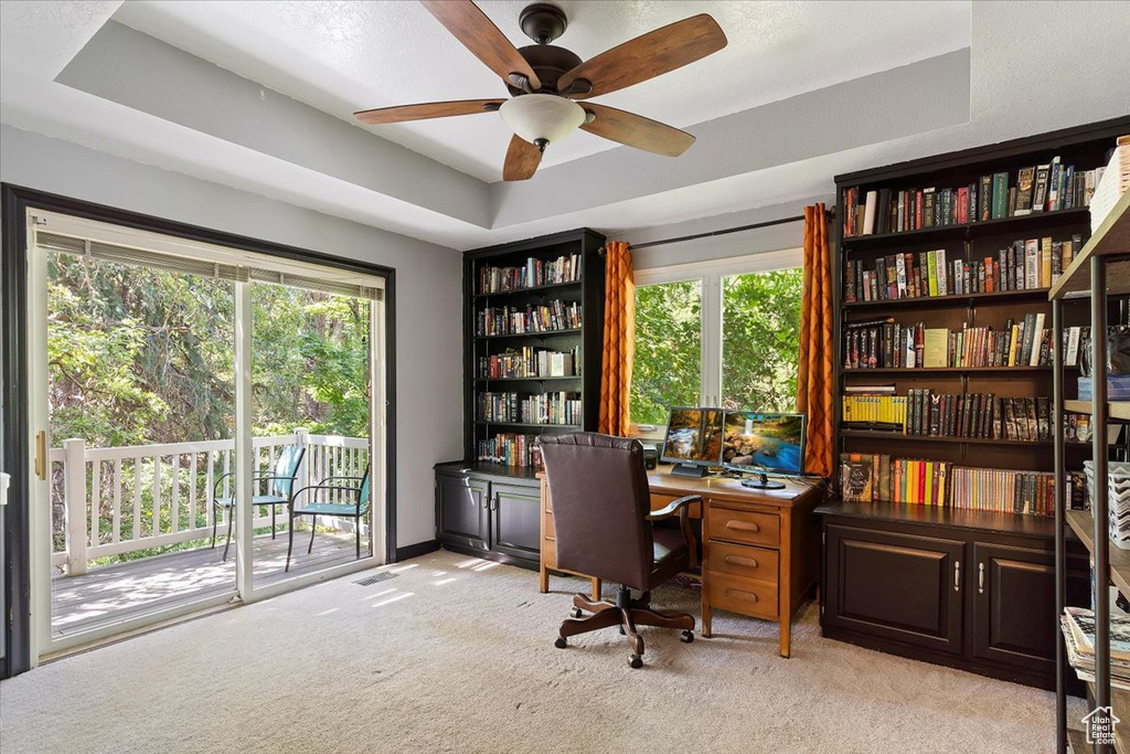 Office space featuring ceiling fan, light colored carpet, and a tray ceiling