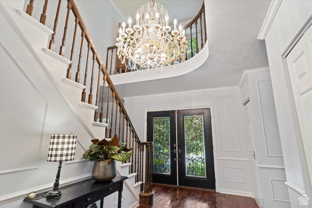 Entrance foyer with french doors, a chandelier, a textured ceiling, dark hardwood / wood-style floors, and ornamental molding