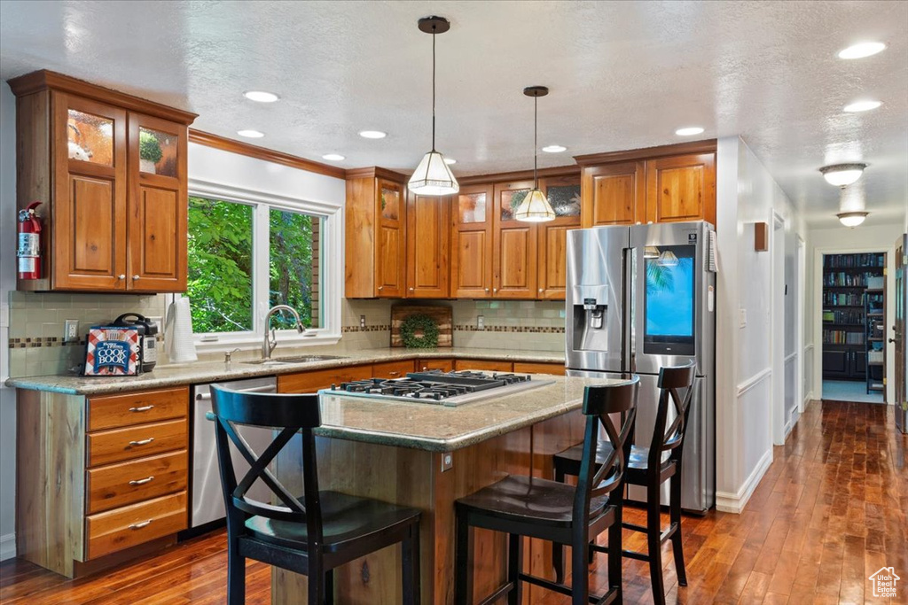 Kitchen with backsplash, dark hardwood / wood-style floors, stainless steel appliances, hanging light fixtures, and sink