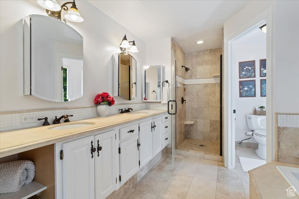 Bathroom with tile patterned floors, tasteful backsplash, a tile shower, dual bowl vanity, and toilet