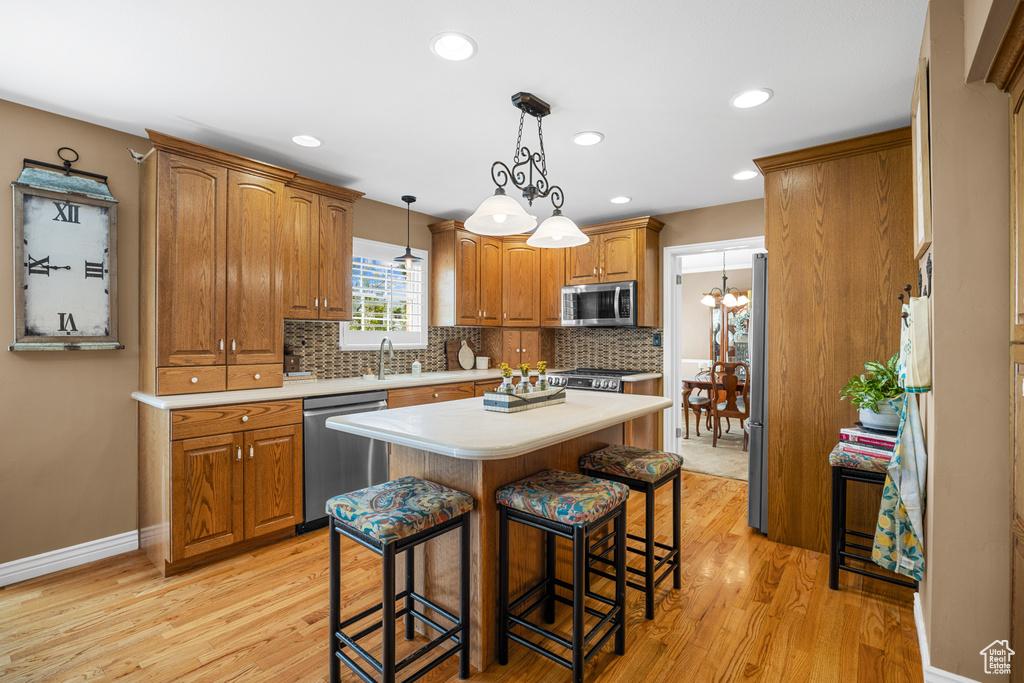 Kitchen featuring appliances with stainless steel finishes, pendant lighting, backsplash, light wood-type flooring, and a center island