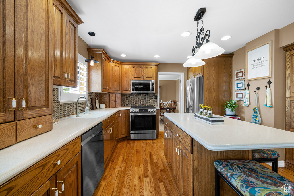 Kitchen with light hardwood / wood-style flooring, stainless steel appliances, sink, hanging light fixtures, and decorative backsplash