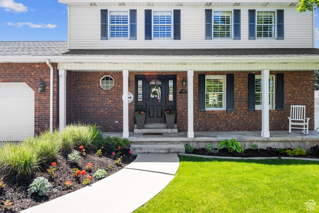 View of exterior entry featuring a porch, a garage, and a yard