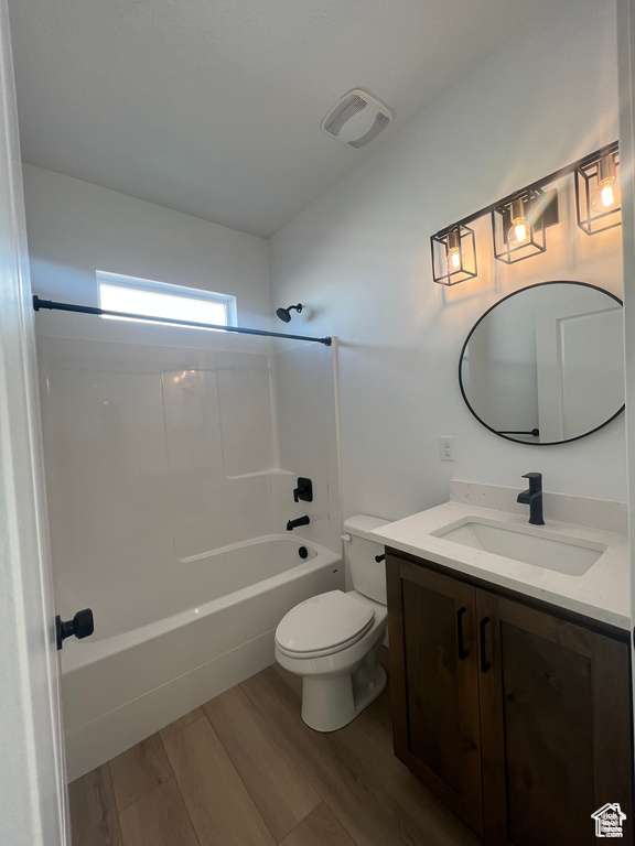 Full bathroom with wood-type flooring, large vanity, toilet, and tub / shower combination