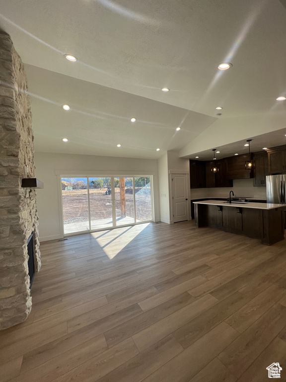 Unfurnished living room featuring sink, vaulted ceiling, a fireplace, and wood-type flooring