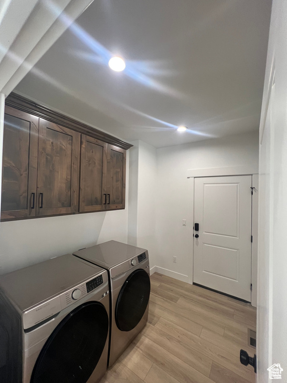 Washroom featuring cabinets, light wood-type flooring, and washing machine and clothes dryer