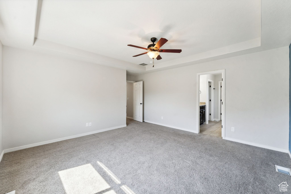 Carpeted empty room with a raised ceiling and ceiling fan