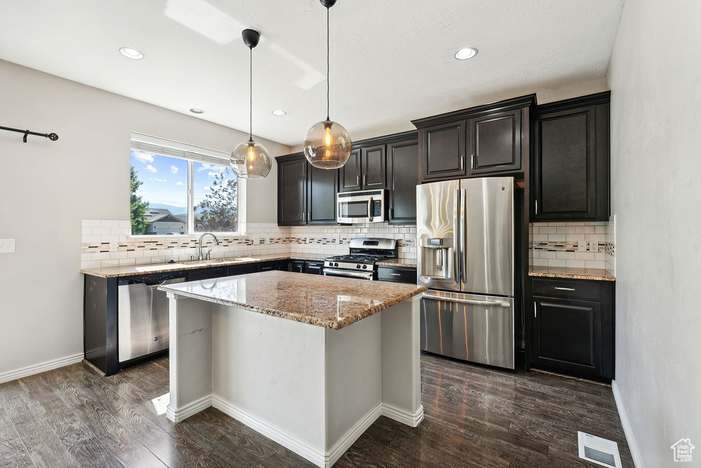 Kitchen with dark hardwood / wood-style flooring, a kitchen island, hanging light fixtures, appliances with stainless steel finishes, and sink