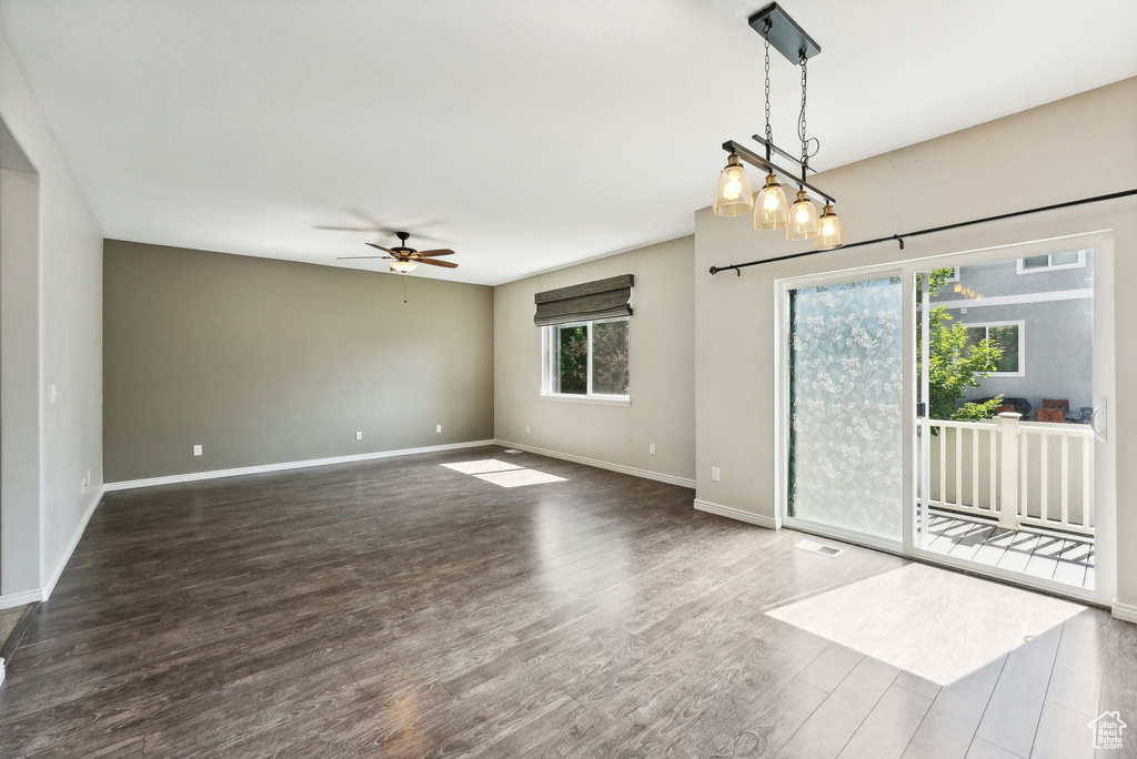 Spare room featuring ceiling fan with notable chandelier and dark hardwood / wood-style floors