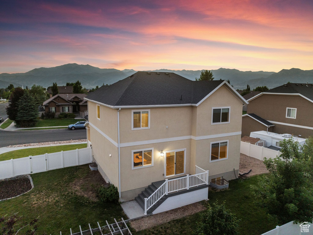 Back house at dusk featuring a mountain view and a lawn