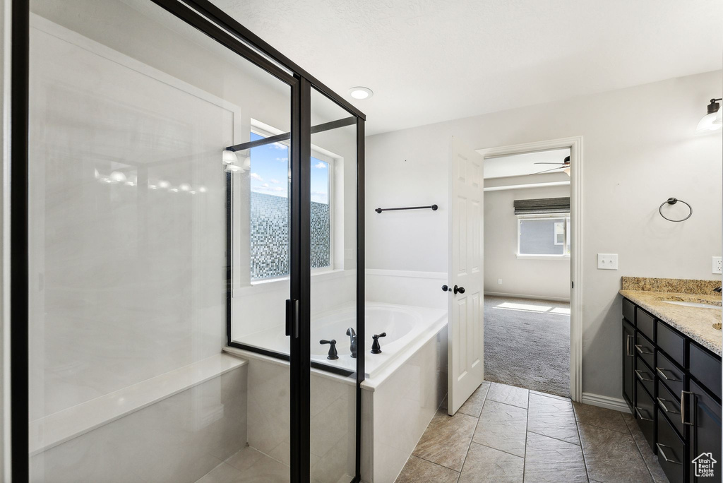 Bathroom featuring a relaxing tiled tub, vanity, tile patterned flooring, and ceiling fan