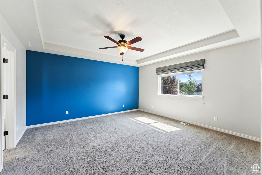 Carpeted empty room featuring ceiling fan and a tray ceiling